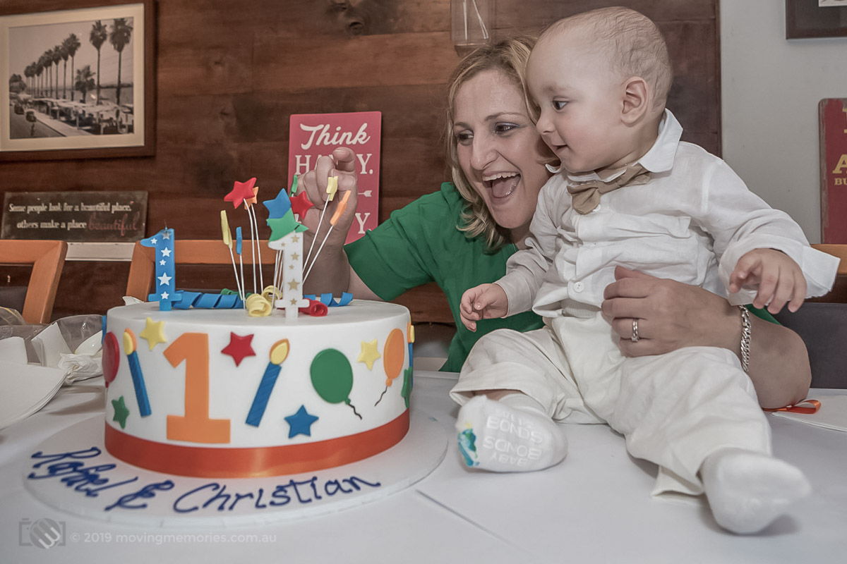 a baby twin boy with his mother takes joy in the sight of his colourful birthday cake also celebrated at the baby's Greek Orthodox Christening reception at Tavernaki Greek Restaurant Sydney
